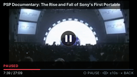 Pocket YouTube on a PSP: a video paused under a centered pause badge, with the title bar, red progress bar and playback hints of the player HUD.